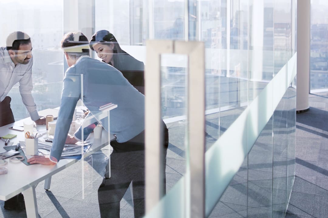 Three colleagues discussing plans, standing around a conference table.